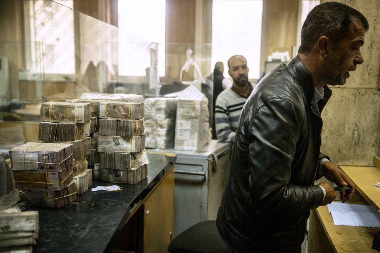 موظف يعمل أمام أكوام من الليرات السورية في قسم الصرافة بالبنك المركزي السوري (غيتي)