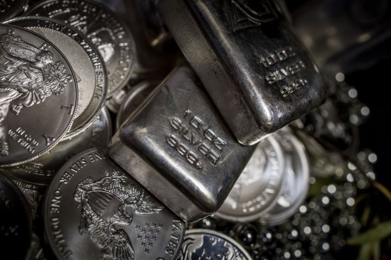 Multiple stacks of 10 ounce Silver bullion Ingot bars and 1 ounce Silver dollar coins among piles of silver ball bearings against a black background featuring the 2016 American Eagle US one dollar coin, the 2021 South African Krugerrand, the 2021 Australian Kangaroo, the 2013 Weiner Philharmonika, the 2020 Scottsdale Reserve Lion and the 2020 Sunshine Minting flying Eagle