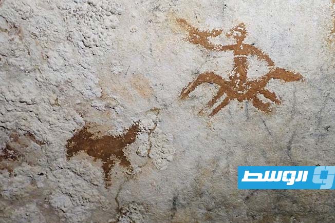 Cave drawings in Sulawesi, Indonesia, depicting a human figure and a bird, with a faint hand stencil in between.