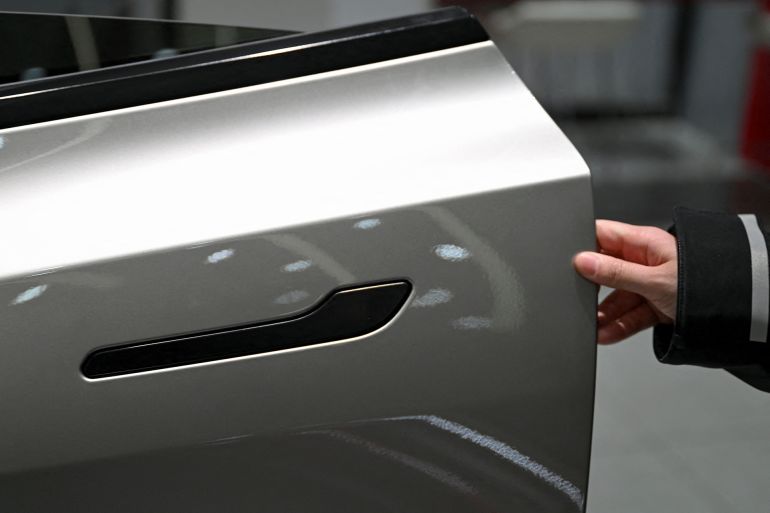 A woman opens the door for a Tesla Model YL electric vehicle at a showroom in Beijing on February 3, 2026. China will ban hidden door handles on cars sold in the country from next year, phasing out the minimalist design popularised by Tesla over safety concerns. (Photo by Pedro Pardo / AFP)